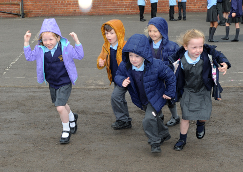 a group of primary school children running excitedly across a playground