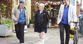 Three older adults walking and talking along a pavement, one is pushing a bike.